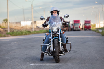 European female motorcyclist sitting on a classic chopper on an asphalt road, front view