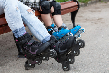 Plakat Close-up view at the in-line skates wearing on mother and children legs, people sitting on the bench