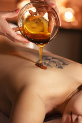 Beautiful young woman in spa salon having massage therapy with honey procedure