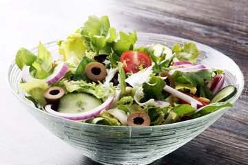 bowl of salad with vegetables and greens on wooden table