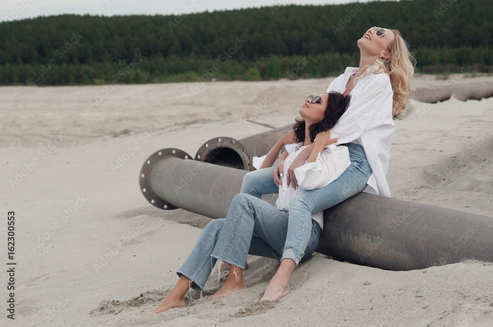 Wall mural Romantic moment of the two girls are lovers to each other. They sit on the beach and laughing