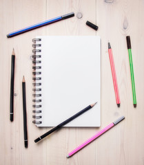 concept of desktop for drawing sketches, notebook with white sheets spread around colored pencils and pens, space for text, border, on a white wooden table