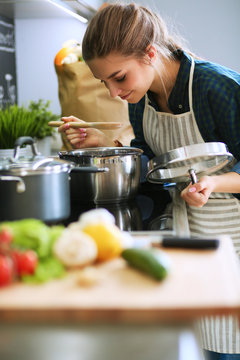 Young woman standing by the stove in the kitchen .