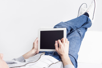 Modern Technology Ideas and Concepts. Portrait of Relaxed Caucasian Man Working with Tablet Computer while Lying on Floor with Legs Lifted on Box in Front.
