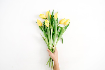 Female hand holding beautiful yellow tulip flowers bouquet on white background. Flat lay, top view.