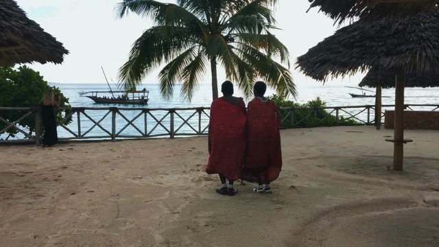 Two Masai people dances their national African dance on the Indian Ocean beach at sunset and bids farewell to the sun. Tanzania. Zanzibar. Slow motion. 4K.