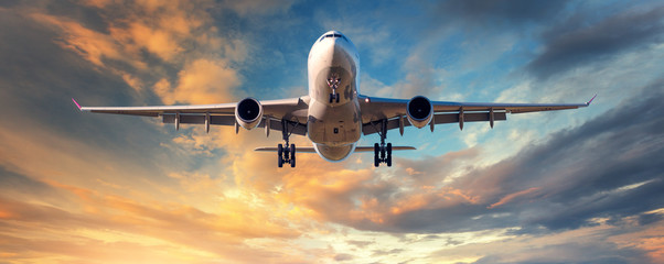 Landend vliegtuig. Landschap met wit passagiersvliegtuig vliegt in de blauwe lucht met wolken bij kleurrijke zonsondergang. Reizen achtergrond. Passagiersvliegtuig. Zakenreis. Commerciële vliegtuigen. Concept