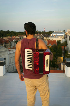 Young man with accordion on roof terrace overlooking the town