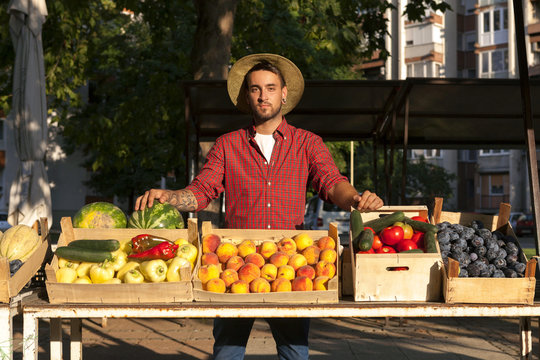 Young Man Selling Fruit And Vegetables At Market Stall