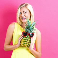 Happy young woman holding a pineapple on a pink background