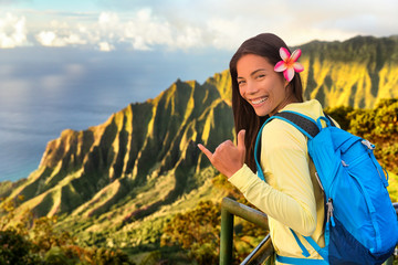 Hawaii hiker girl tourist doing shaka hawaiian hand sign at Na pali lookout in Kauai, Hawaii. Travel Asian woman backpacker hiking with bag at famous destination Kalalau hawaiian attraction. - obrazy, fototapety, plakaty