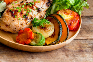 Homemade chicken breast barbecue on wood plate served with grilled vegetables. Delicious chicken barbecue and grilled vegetables for lunch or dinner. Roast chicken breast on rustic wood table.