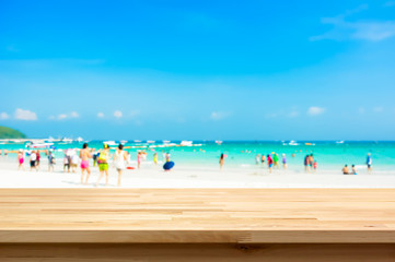 Wood table top on blur beach background with people in colorful clothes
