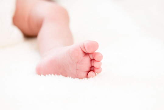 Small little foot of newborn baby on white wool fluff sheet
