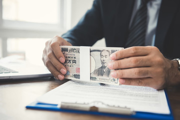 Businessman holding money, Japanese yen bills, on working table