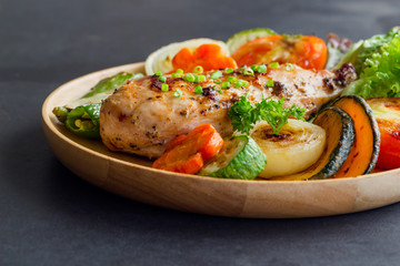 Homemade chicken breast barbecue on wood plate served with grilled vegetables. Delicious chicken barbecue and grilled vegetables for lunch or dinner. Roast chicken breast on granite table.