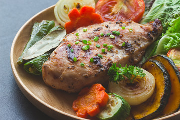 Homemade chicken breast barbecue on wood plate served with grilled vegetables. Delicious chicken barbecue and grilled vegetables for lunch or dinner. Roast chicken breast on granite table.