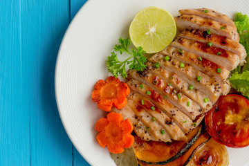 Sliced chicken breast barbecue on white plate served with grilled vegetable. Delicious  chicken breast steak and salad for dinner. Homemade chicken breast barbecue on blue wood table for background.