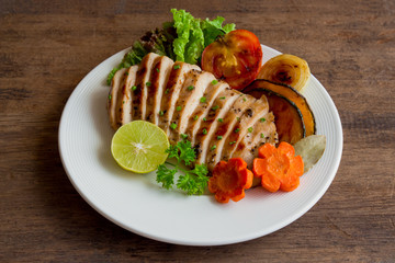Sliced chicken breast barbecue on white plate served with grilled vegetable. Delicious  chicken breast steak and salad for dinner. Homemade chicken breast barbecue on wood table for background.