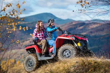 Fototapeta na wymiar Happy females ATV driver in winter clothing on snowy hills on the background of mighty mountains and trees with yellow leaves
