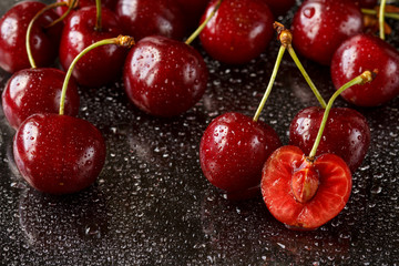 Close up of half sliced and whole cherries on a black background with water drops