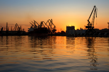 Fototapeta na wymiar Beautiful sunset behind Seaport Varna, Bulgaria. Silhouettes of industrial cranes and buildings with reflections in the water