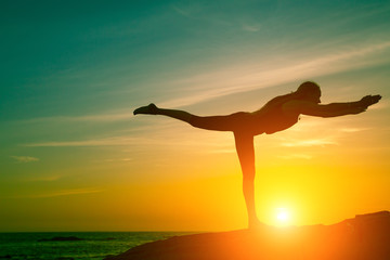 Yoga and healthy lifestyle. Silhouette of fitness woman doing exercises on the sea beach during amazing sunset.
