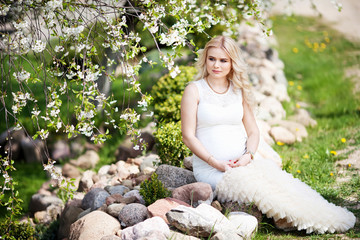 Portrait of beautiful pregnant woman in the flowering park. Young happy pregnant woman relaxing in nature.