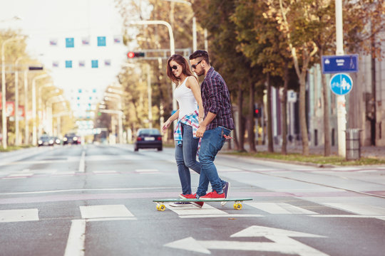 Young couple skateboarding over zebra crossing