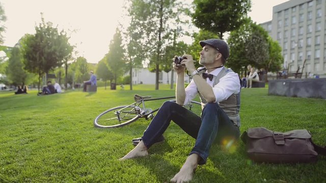 Mature businessman with camera and bicycle in the city park.
