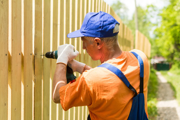 Handyman outdoors works with cordless screwdriver, mounting wooden fence