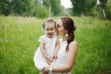 Young mother with daughter on hands in the same white dresses in the Park. Family Look