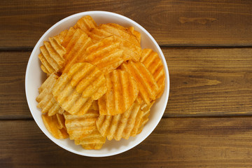 Potato chips in bowl on a wooden background, top view