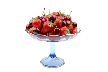 Strawberries and cherries in glass stand isolated on white background. Fruits strawberries and cherries in blue glass bowl.