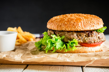Classic tasty hamburger with tasty beef, sauce and french fries on dark background. American food