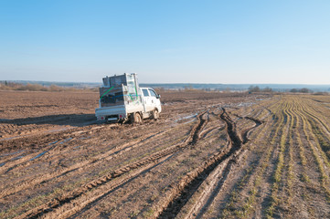 Off-road truck with furniture settles down in mud on dirt road in fallow field
