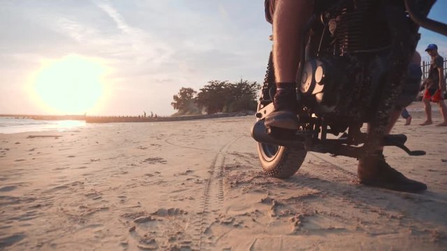 Dolly shot of motorcyclist and his motorbike on the road during sunset