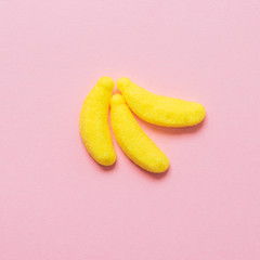 three yellow sugar candy or jelly beans in the shape of a banana on a pink background. minimal concept of food