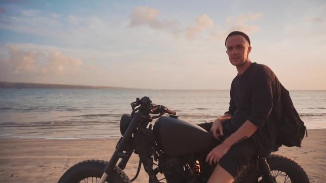 Dolly shot of motorcyclist and his motorbike on the road during sunset
