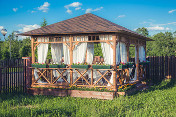 Outdoor wooden gazebo with flowers and summer landscape background