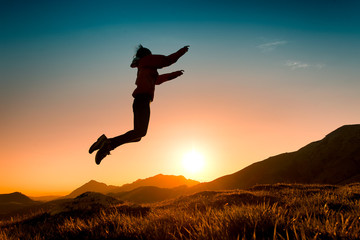 55/5000.Girl jumps in the meadow during a sunset in the mountains