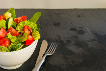 Lettuce leaves, cherry tomatoes, cucumber and broccoli salad on dark background.