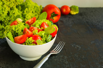 Lettuce leaves, cherry tomatoes, cucumber and broccoli salad on dark background.