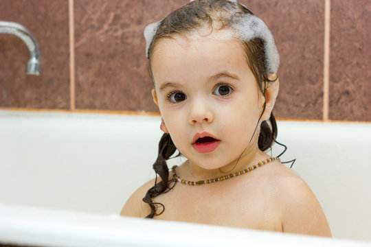 Little kid girl having fun in bathroom with foam on her hairs