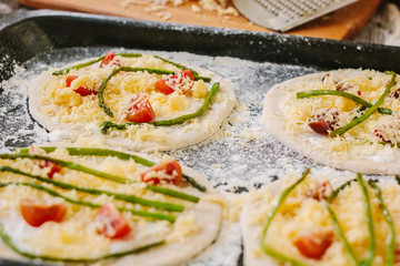 Cooking process of making mini pizza - small and personal, with cheese, tomatoes and asparagus.
