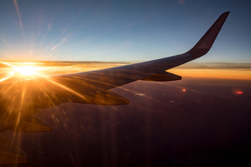 Sun flare over wing of plane flying at dusk