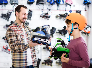Male shop assistant helping boy to choose roller-skates in sports store