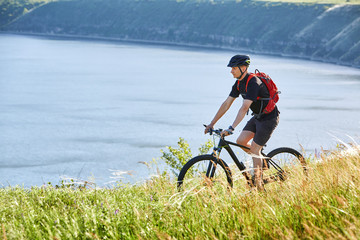 Attractive cyclist riding the mountain bike on the summer trail above the river.