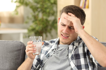 Man suffering head ache holding a painkiller glass