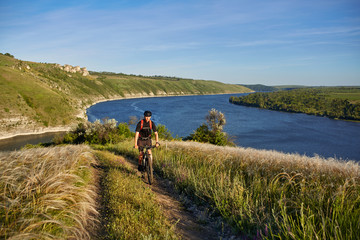 Fototapeta premium Attractive cyclist riding the mountain bike on the summer trail above the river.